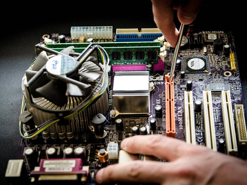 Hand mit Schraubendreher an einem ausgebauten Mainboard mit CPU-Kühler